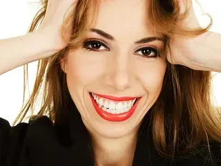 Una mujer con lápiz labial rojo sonríe y sostiene su cabello.