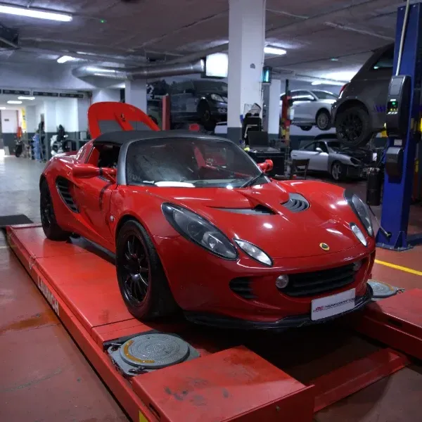 Coche deportivo rojo sobre un elevador en un taller mecánico, con el capó abierto.