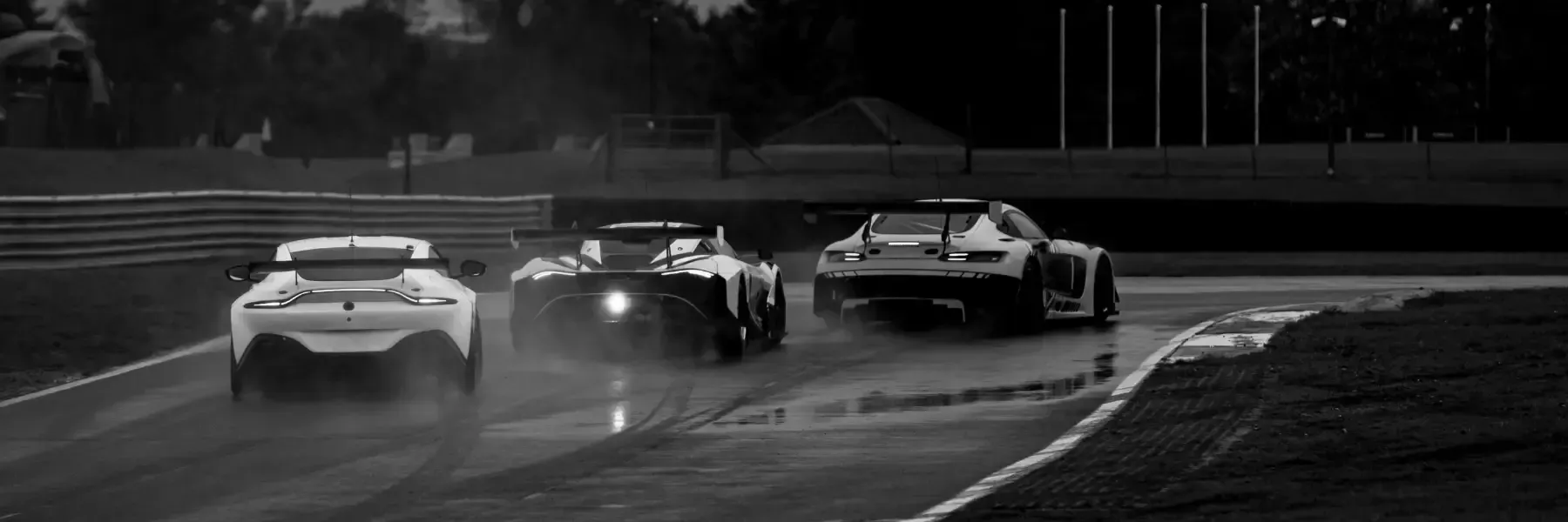 Tres coches de carreras circulando por una pista mojada al anochecer, vistos desde atrás.
