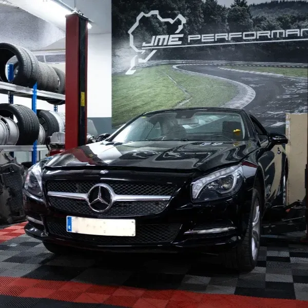 Un Mercedes-Benz negro en un taller mecánico, con neumáticos apilados junto a un elevador de servicio.