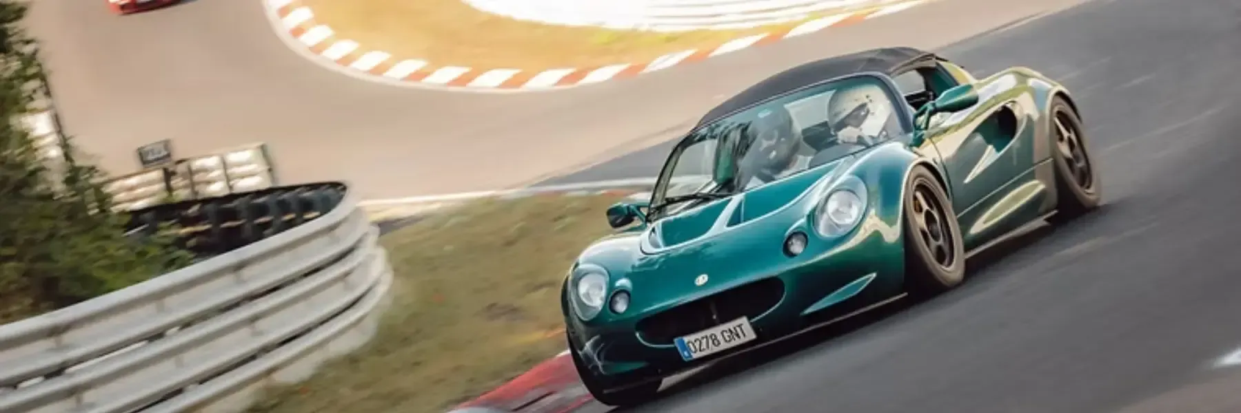 Un deportivo Lotus de color verde oscuro circulando a gran velocidad en una curva de un circuito de carreras.