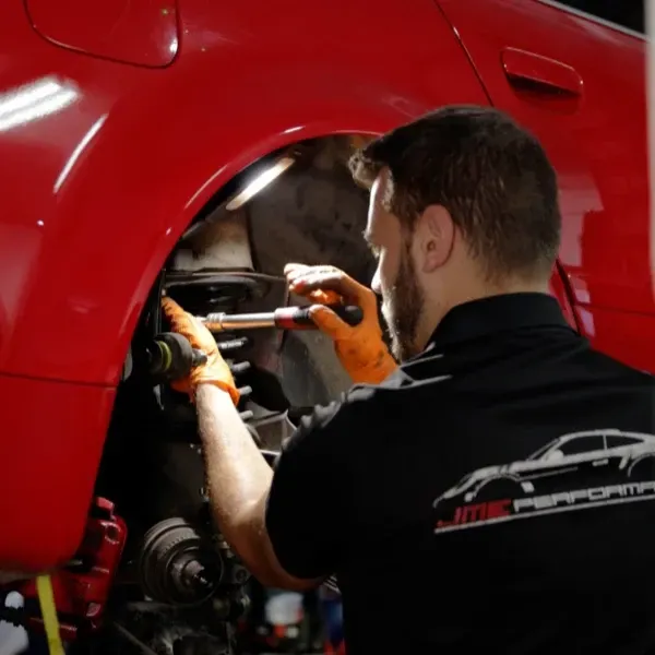 Mecánico con guantes naranjas trabajando en el compartimento del motor de un coche rojo.