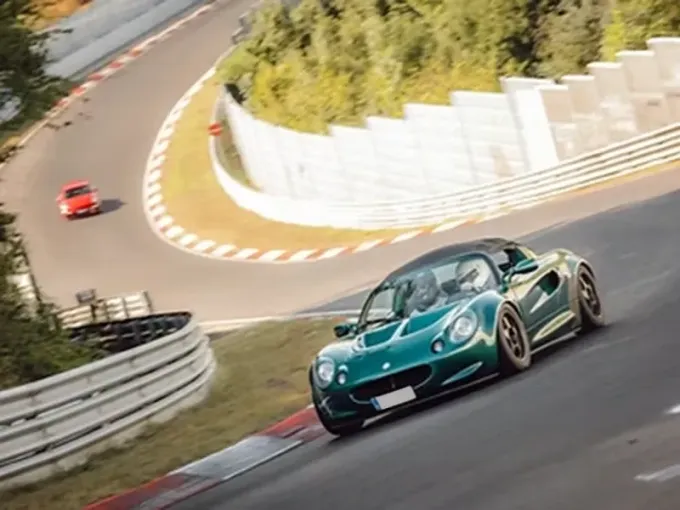 Un deportivo Lotus verde toma una curva a gran velocidad en un circuito de carreras, con dos ocupantes