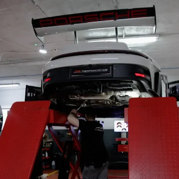 Porsche rojo en un elevador en un taller mecánico, un mecánico trabajando debajo entre dos rampas rojas.