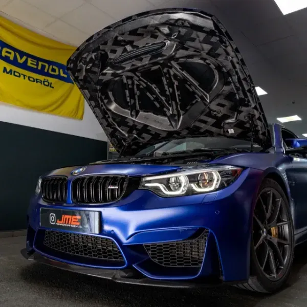 BMW deportivo azul con el capó abierto en un garaje, vista frontal, llantas personalizadas y parrilla no original.