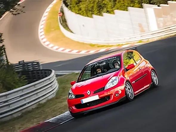 Un Renault Clio rojo circulando por un circuito, tomando una curva con dos personas en su interior.