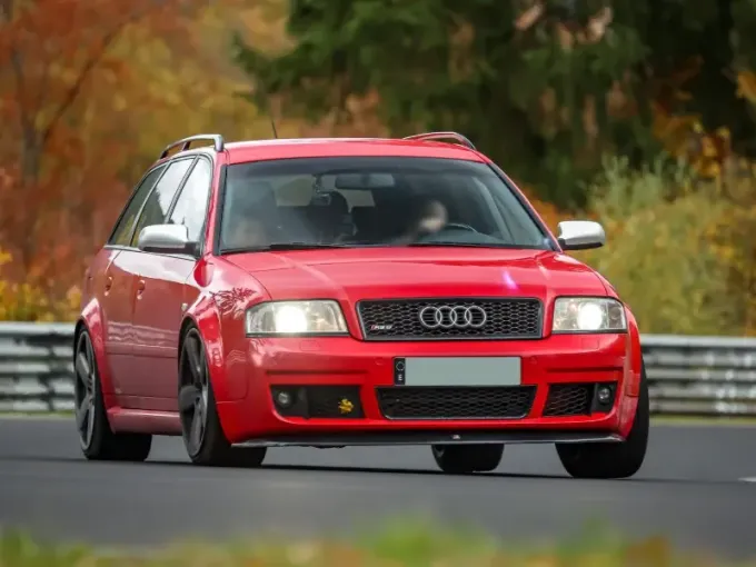Tres coches de carreras circulando por una pista mojada al anochecer, vistos desde atrás.