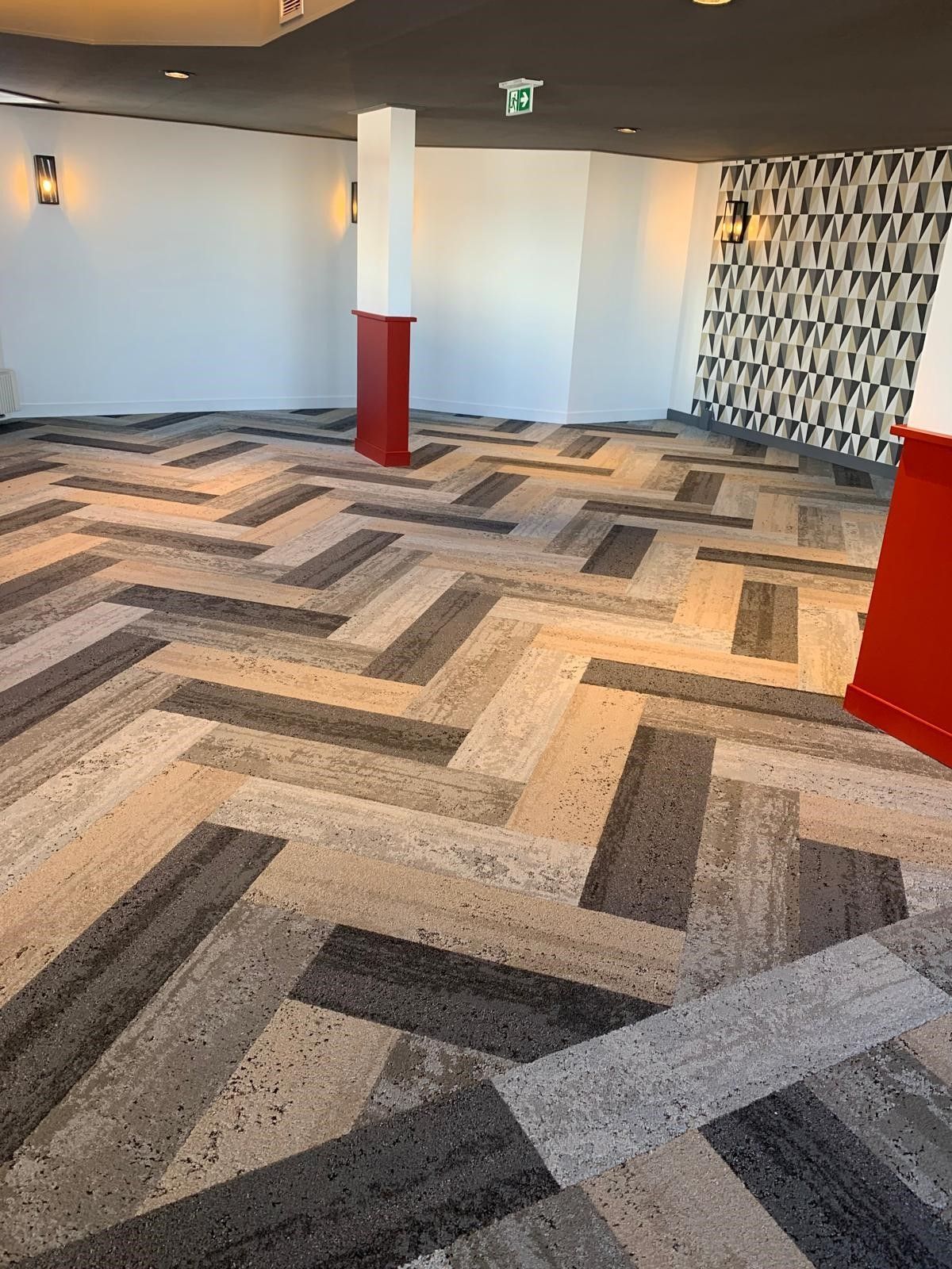 Hall d'entrée moderne et vide avec moquette à motifs, murs blancs, colonnes rouges et un mur décoratif.
