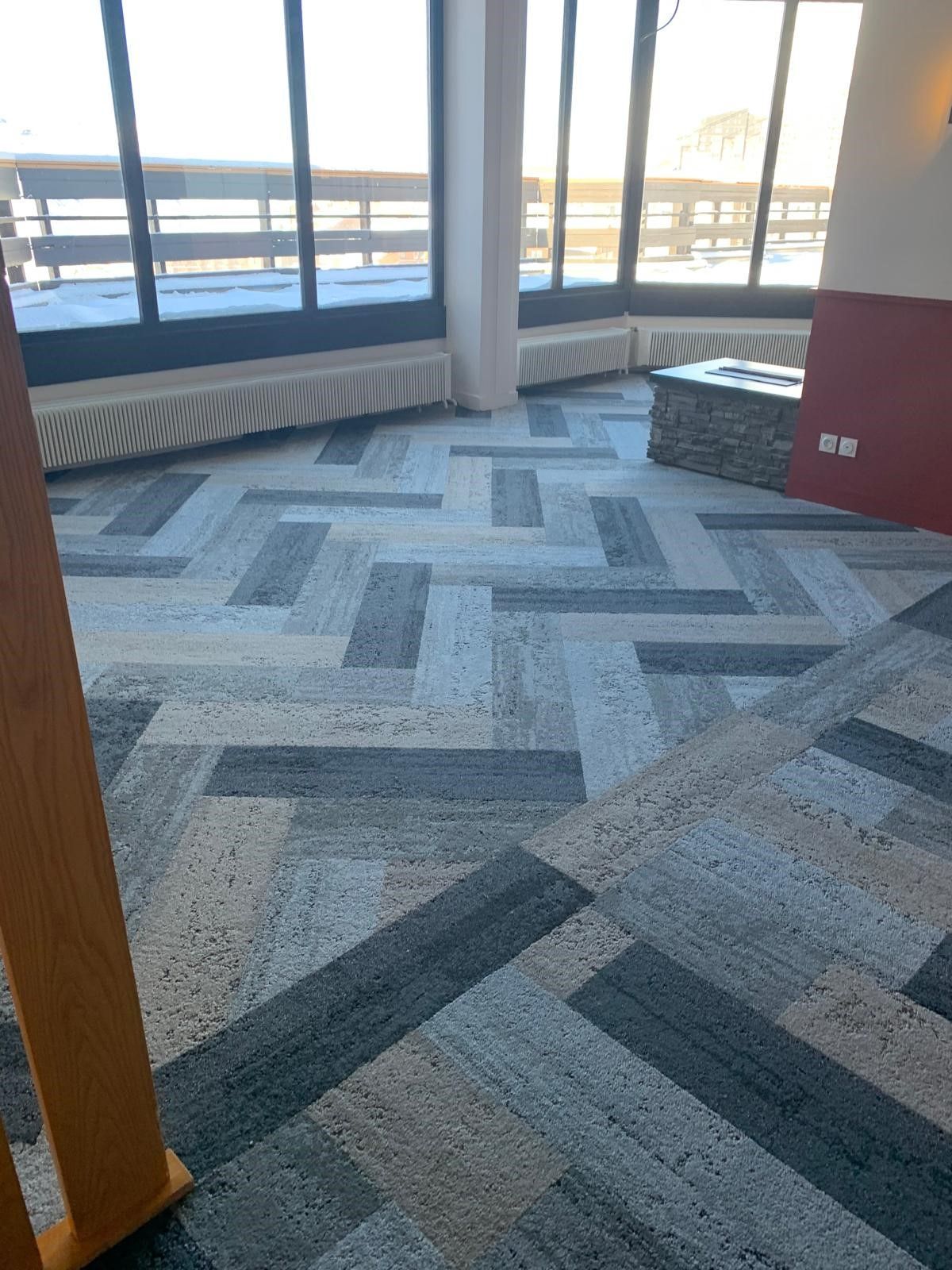 Hall d'entrée recouvert de moquette, avec de grandes fenêtres, de la lumière naturelle et un poteau jaune au premier plan.