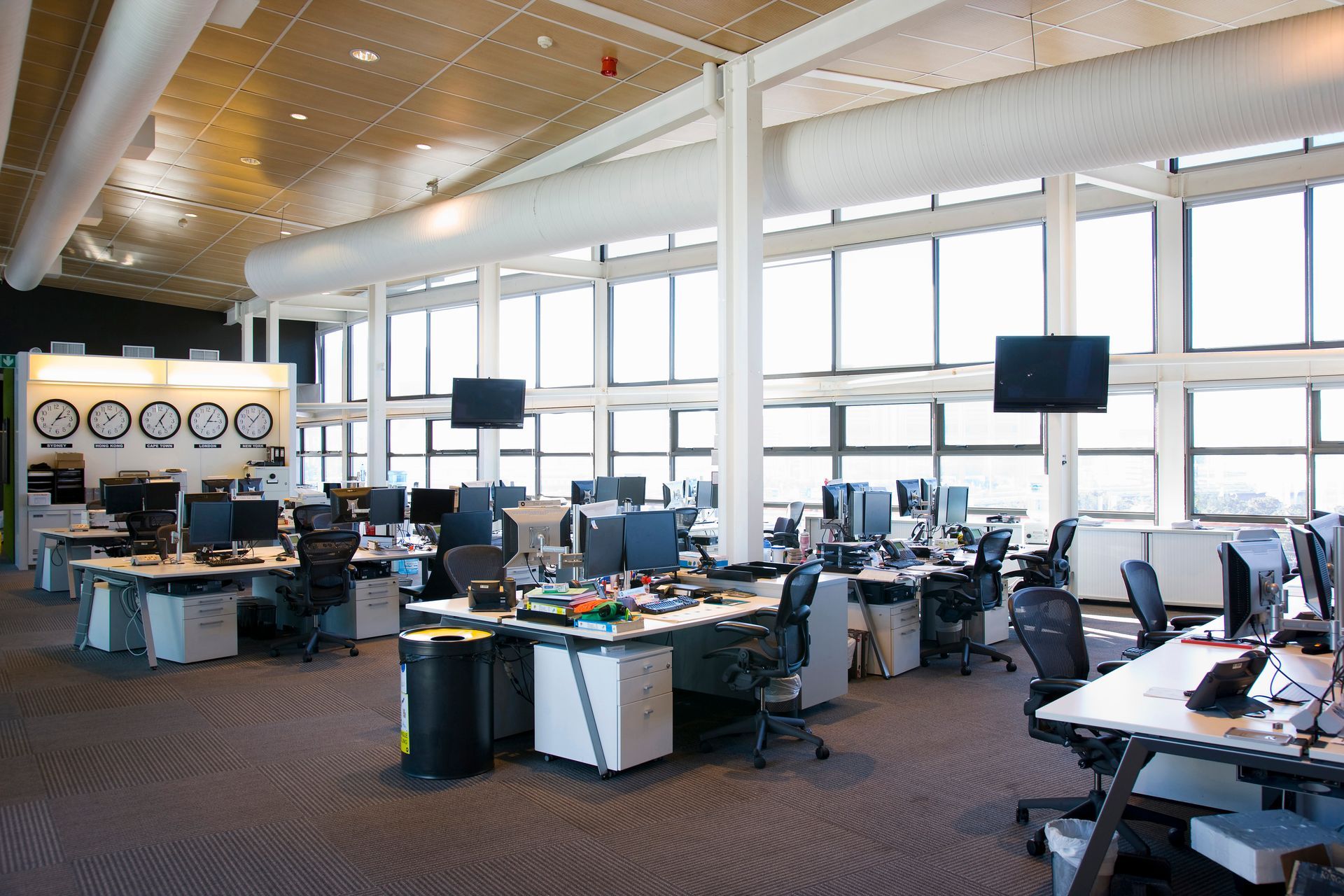 Espace de travail ouvert avec bureaux, ordinateurs et grandes fenêtres.