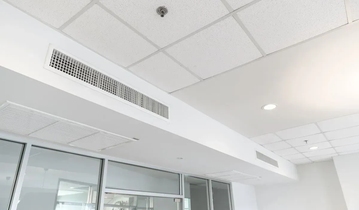 Plafond de bureau lumineux avec aérations, éclairage encastré et parois vitrées en dessous.