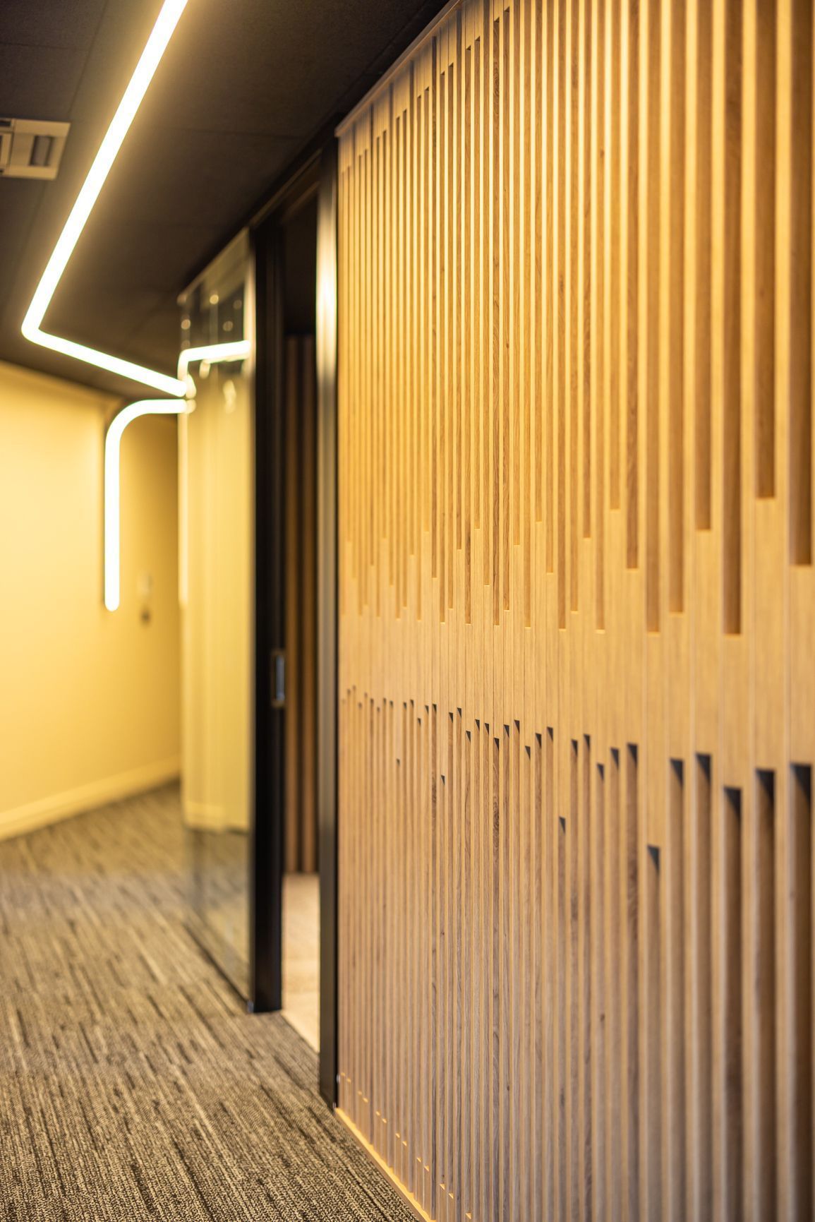 Couloir moderne avec éclairage chaleureux, mur lambrissé et sol recouvert de moquette, vu en perspective.
