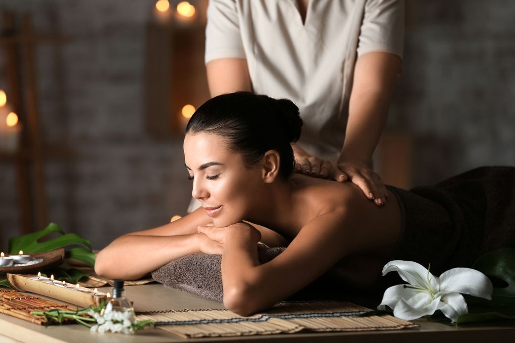 Eine Massagetherapeutin massiert den Rücken eines Klienten auf einer Behandlungsliege mit weissen Handtüchern und Handschuhen.