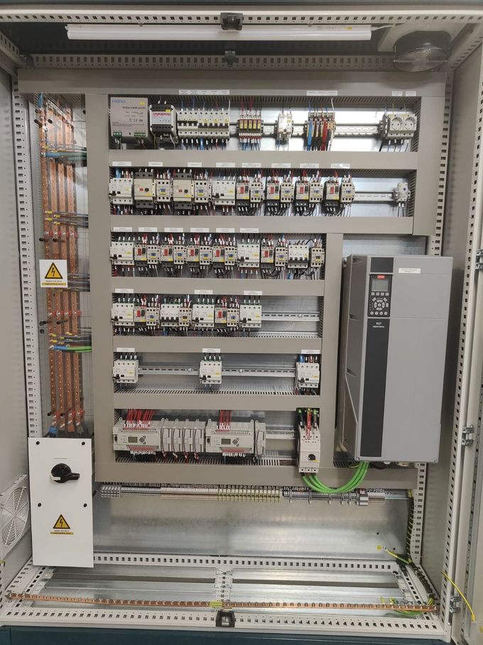 Un panel de control eléctrico abierto con filas de disyuntores, contactores y una gran unidad de accionamiento de color gris.