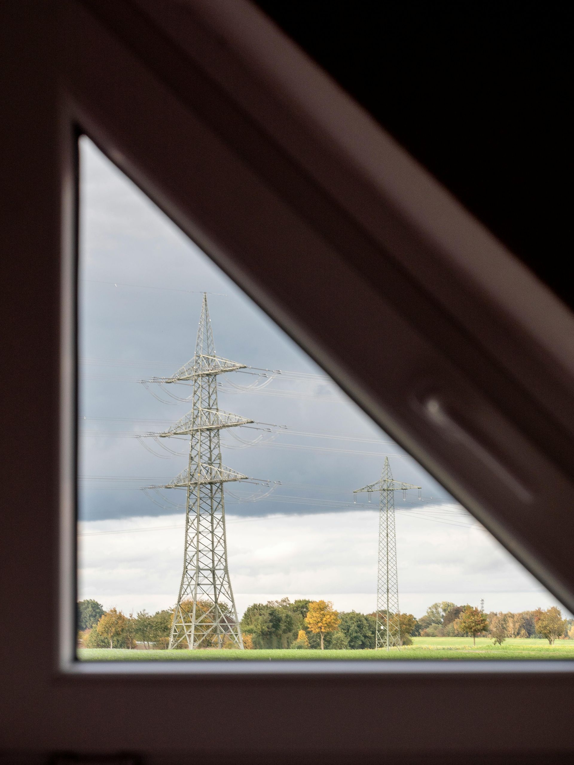Dos torres de transmisión eléctrica se alzan en un campo bajo un cielo nublado, vistas a través de una ventana triangular.