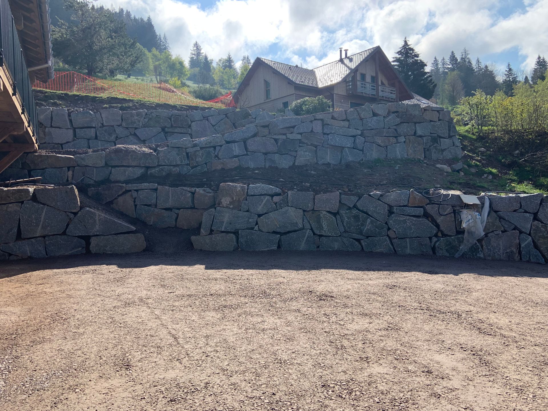Mur de soutènement en pierre avec des maisons et des arbres sur un coteau ensoleillé sous un ciel nuageux