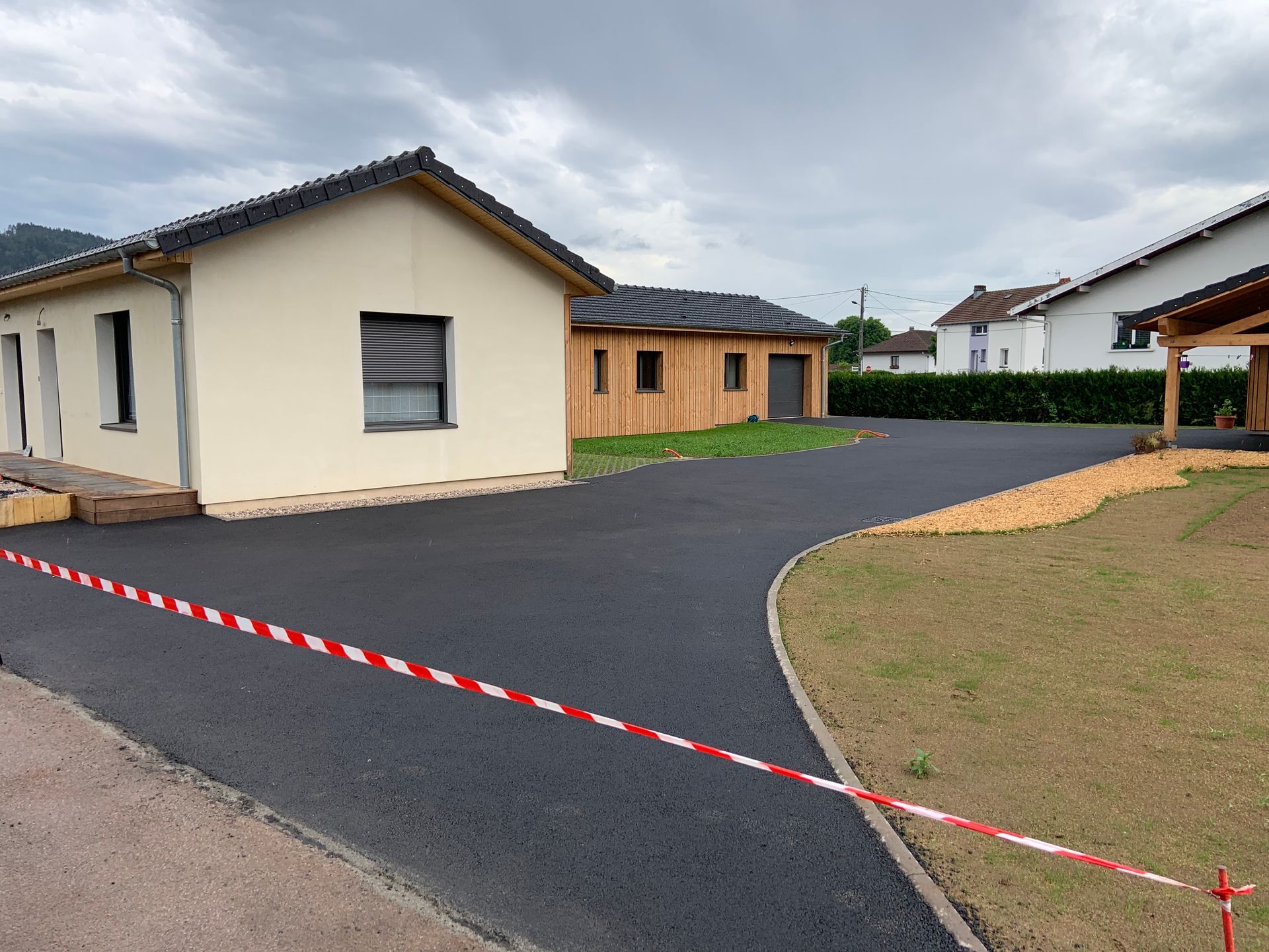 Allée récemment goudronnée à côté de maisons couleur crème et en bois, délimitée par du ruban de signalisation rouge et blanc