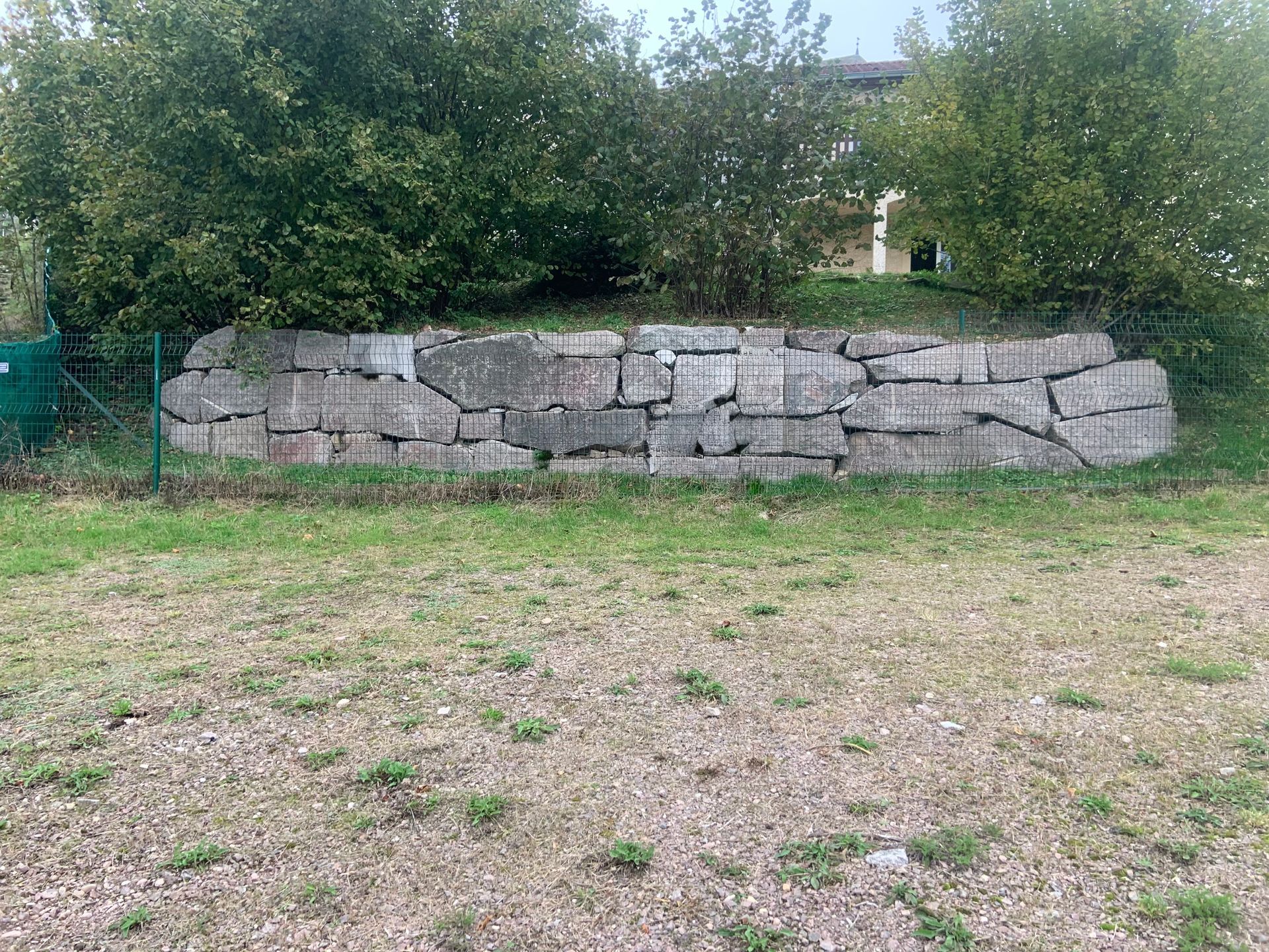 Petit muret de pierre dans un jardin herbeux, avec des arbres et des arbustes en arrière-plan