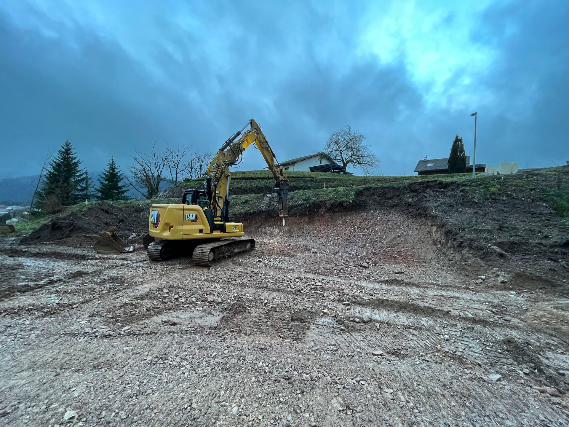 Une pelleteuse jaune sur un chantier boueux sous un ciel bleu nuageux.