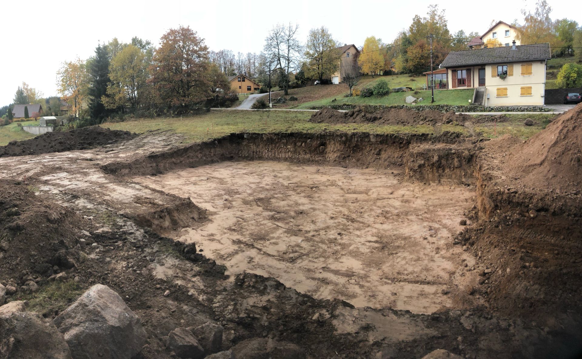Grande excavation boueuse en milieu rural, avec des maisons et des arbres aux couleurs automnales en arrière-plan