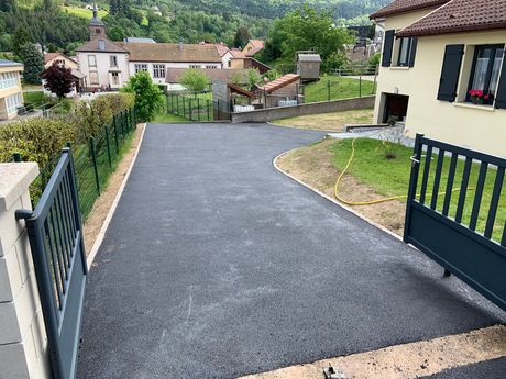 Ouvrez le portail noir qui donne sur une allée récemment pavée, à côté d’une maison surplombant un village en contrebas.