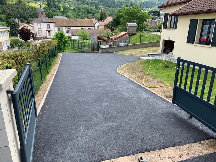 Des piles de gros tuyaux en plastique gris sur un chantier, à côté de gravier et d'herbe.