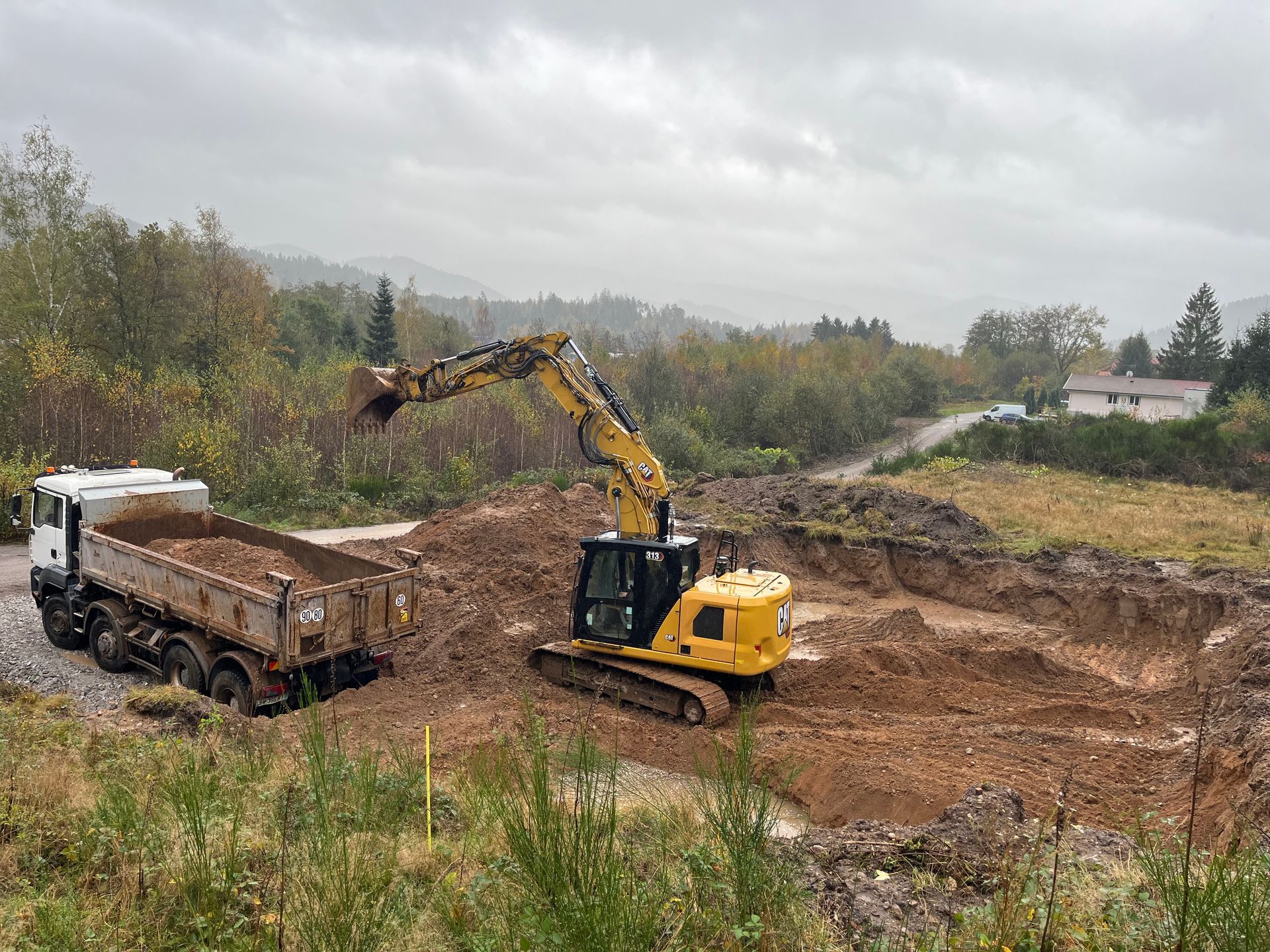 Maison en briques partiellement construite au bord d'une route de campagne sous un ciel nuageux.
