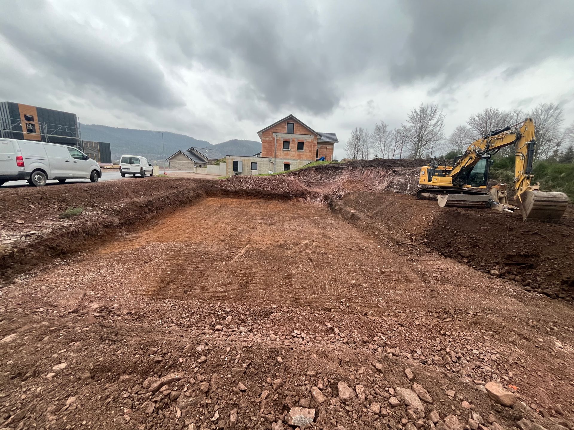 Chantier avec une pelleteuse creusant une grande tranchée au bord d’une route, sous un ciel nuageux