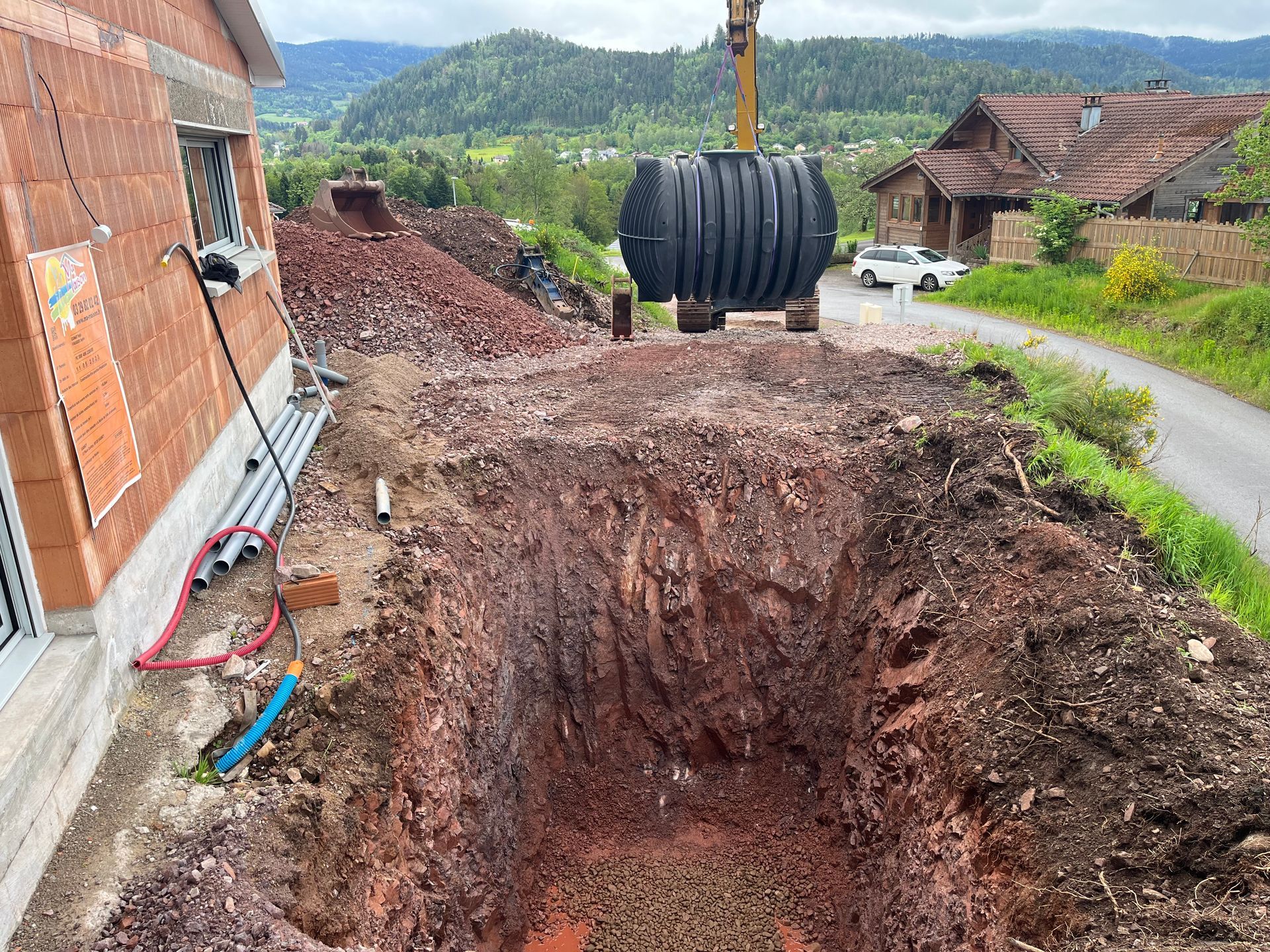 Une grande fosse septique noire est descendue dans une excavation à l'aide de cordes et de supports en bois.