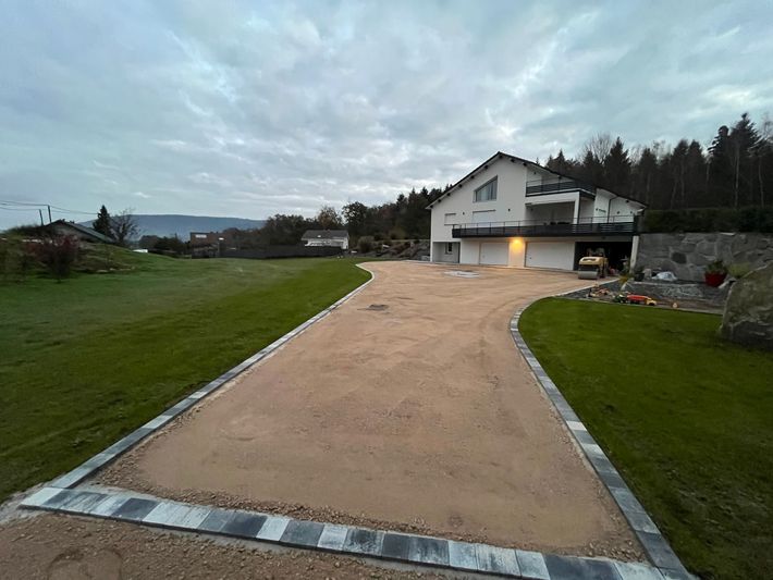 Maison en briques partiellement construite au bord d'une route de campagne sous un ciel nuageux.