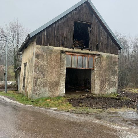 Grange abandonnée et délabrée, aux fenêtres brisées et à la façade supérieure en bois sombre, au bord d'une route.