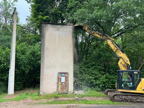 Une pelleteuse jaune près d'un haut mur en béton dans une zone boisée.
