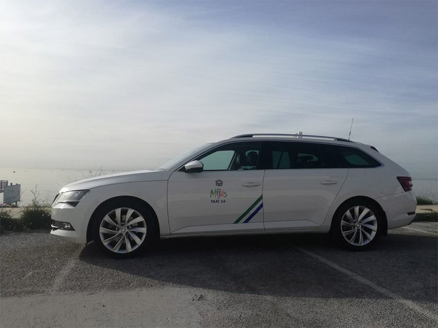 Un coche blanco está aparcado en un estacionamiento con el océano de fondo.