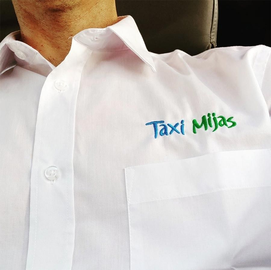 Un hombre que lleva una camisa blanca con el logo de Taxi Mijas bordado.