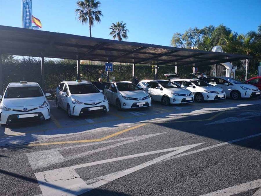 Una fila de coches blancos están aparcados bajo una marquesina al costado de la carretera.