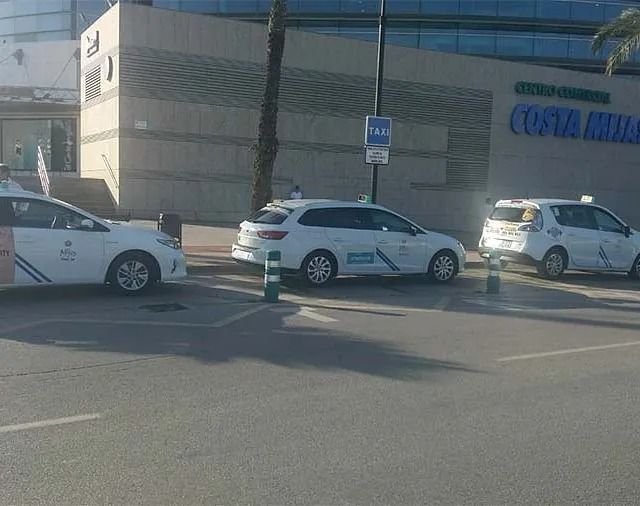 Una fila de taxis están estacionados al costado de la carretera frente a un edificio.