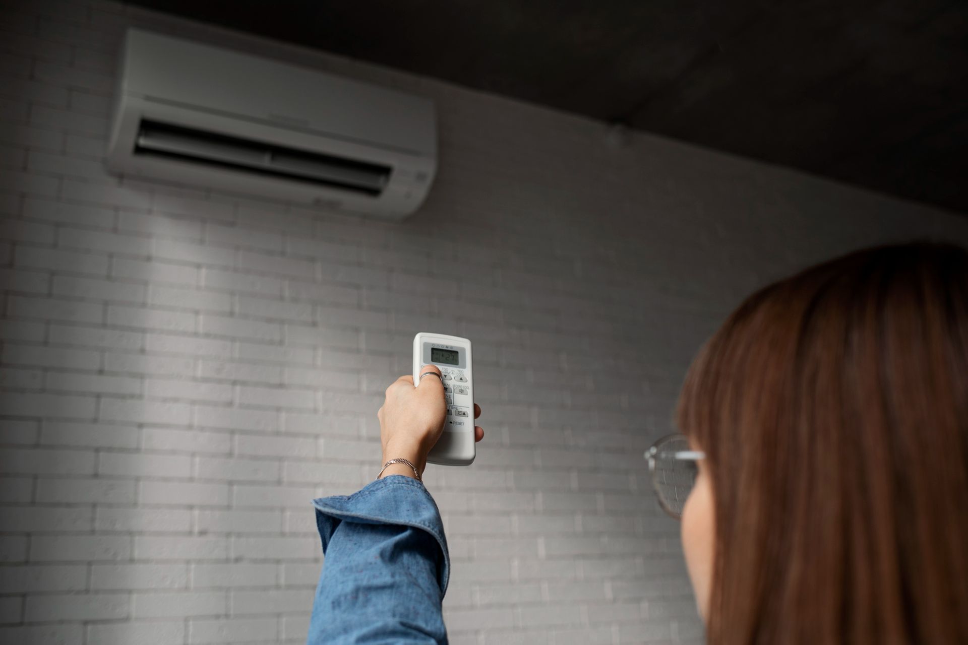 Persona que sostiene un control remoto apuntando a una unidad de aire acondicionado montada en la pared.