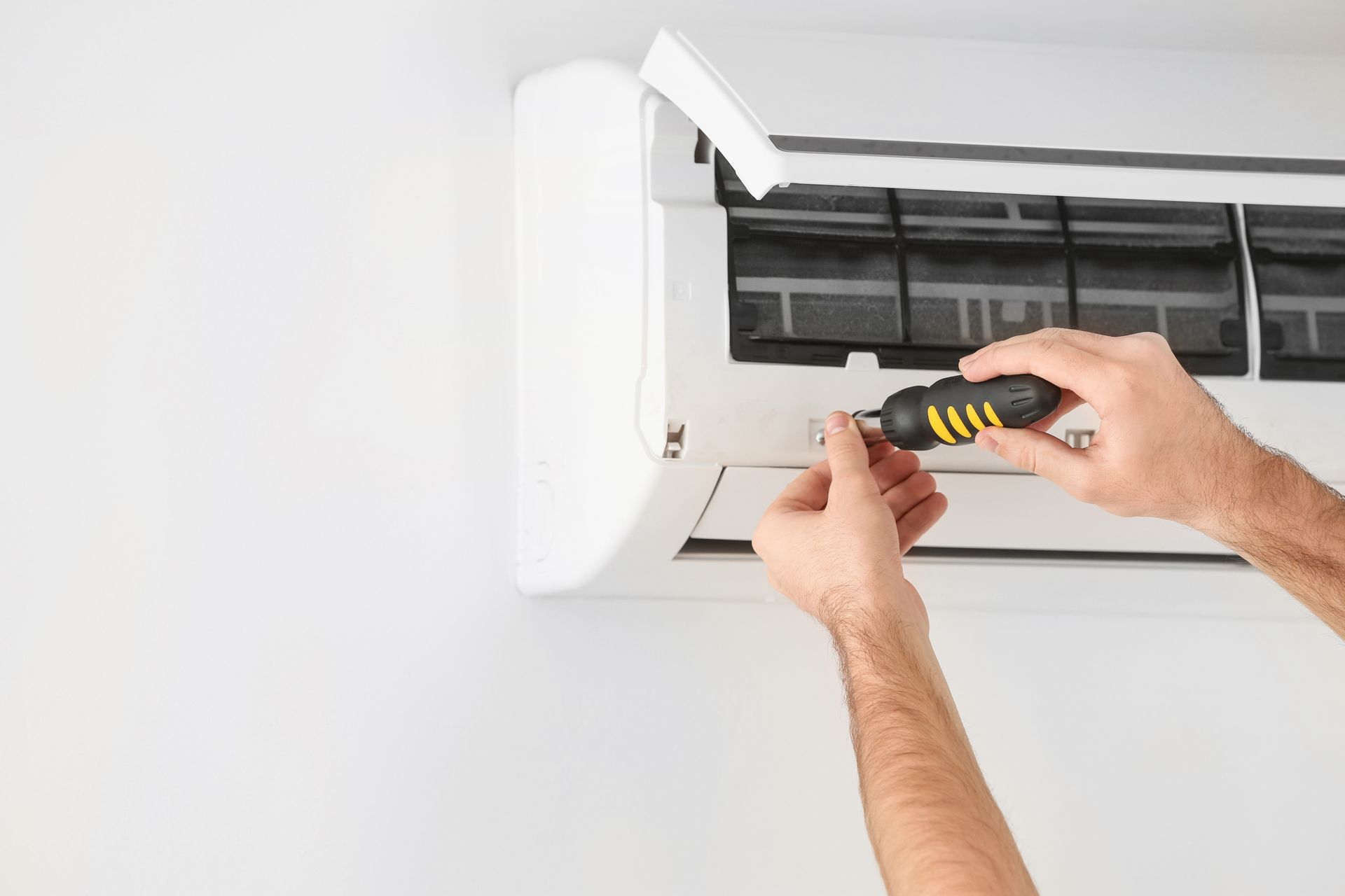 Persona arreglando una unidad de aire acondicionado con un destornillador.