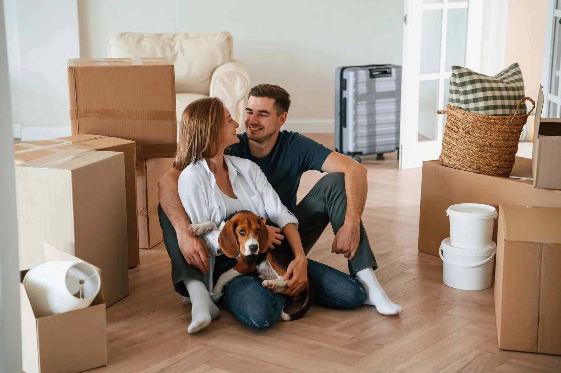 Couple avec un chien beagle se reposant parmi des cartons de déménagement dans une nouvelle maison.