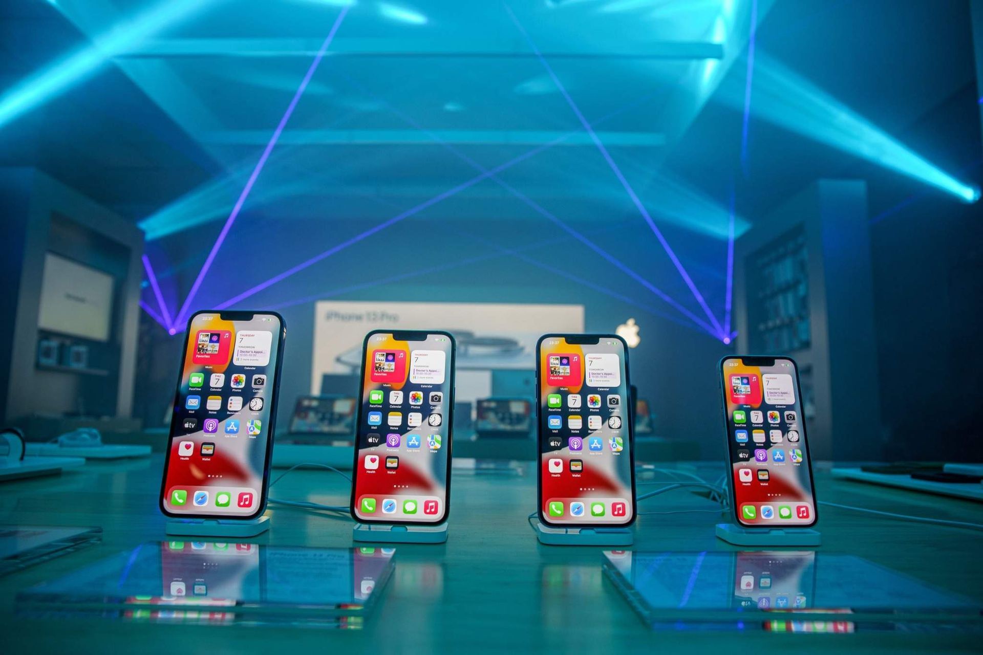 Cuatro teléfonos inteligentes se exhibieron en un escenario brillante con luces láser azules y pantallas de aplicaciones.