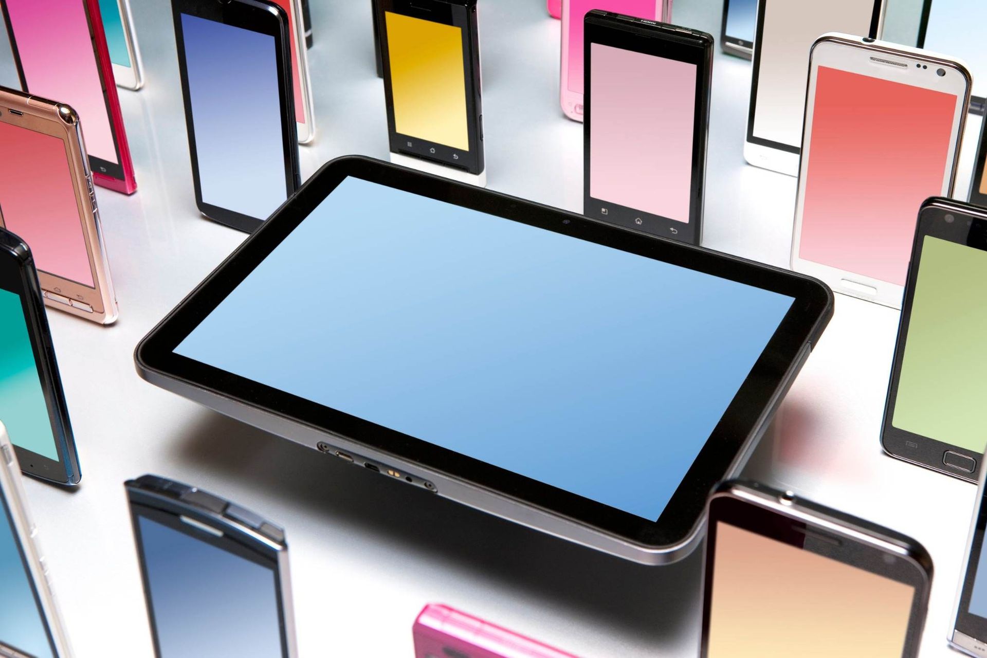 Tableta rodeada de coloridos teléfonos inteligentes sobre un fondo brillante.