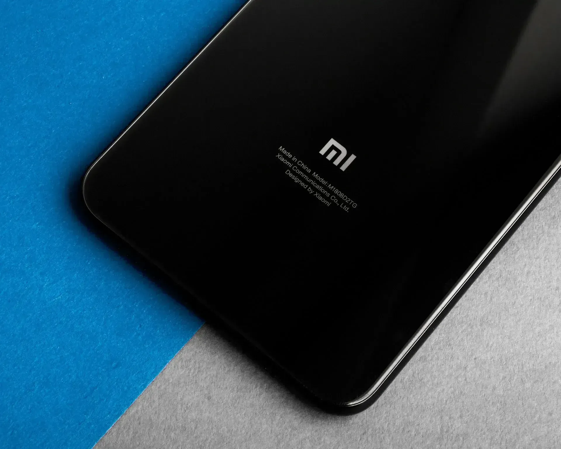 Teléfono Xiaomi negro sobre una superficie azul y gris, mostrando el logotipo trasero.