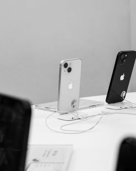 Dos iPhones sobre una mesa blanca con cables de carga, en un entorno de sala de exposición minimalista.