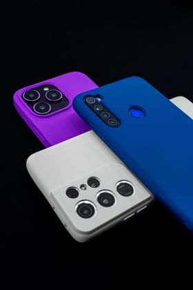 Tres teléfonos inteligentes con fundas de colores (morado, azul y blanco) apilados sobre un fondo negro.