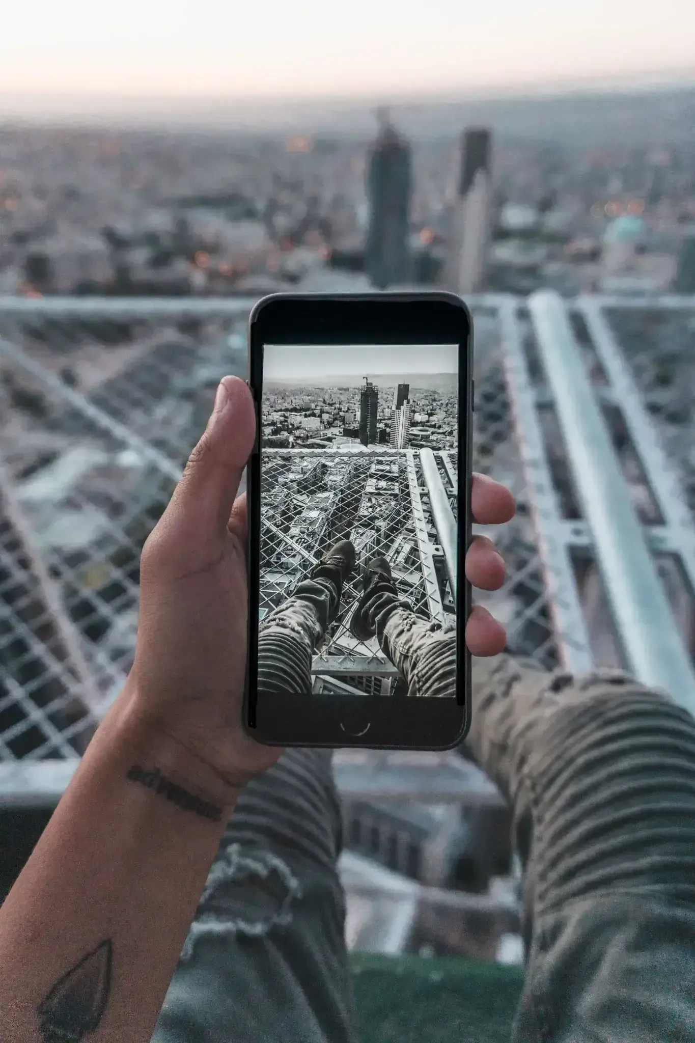 Una mano sostiene un teléfono inteligente que muestra el horizonte de una ciudad desde una azotea al atardecer.