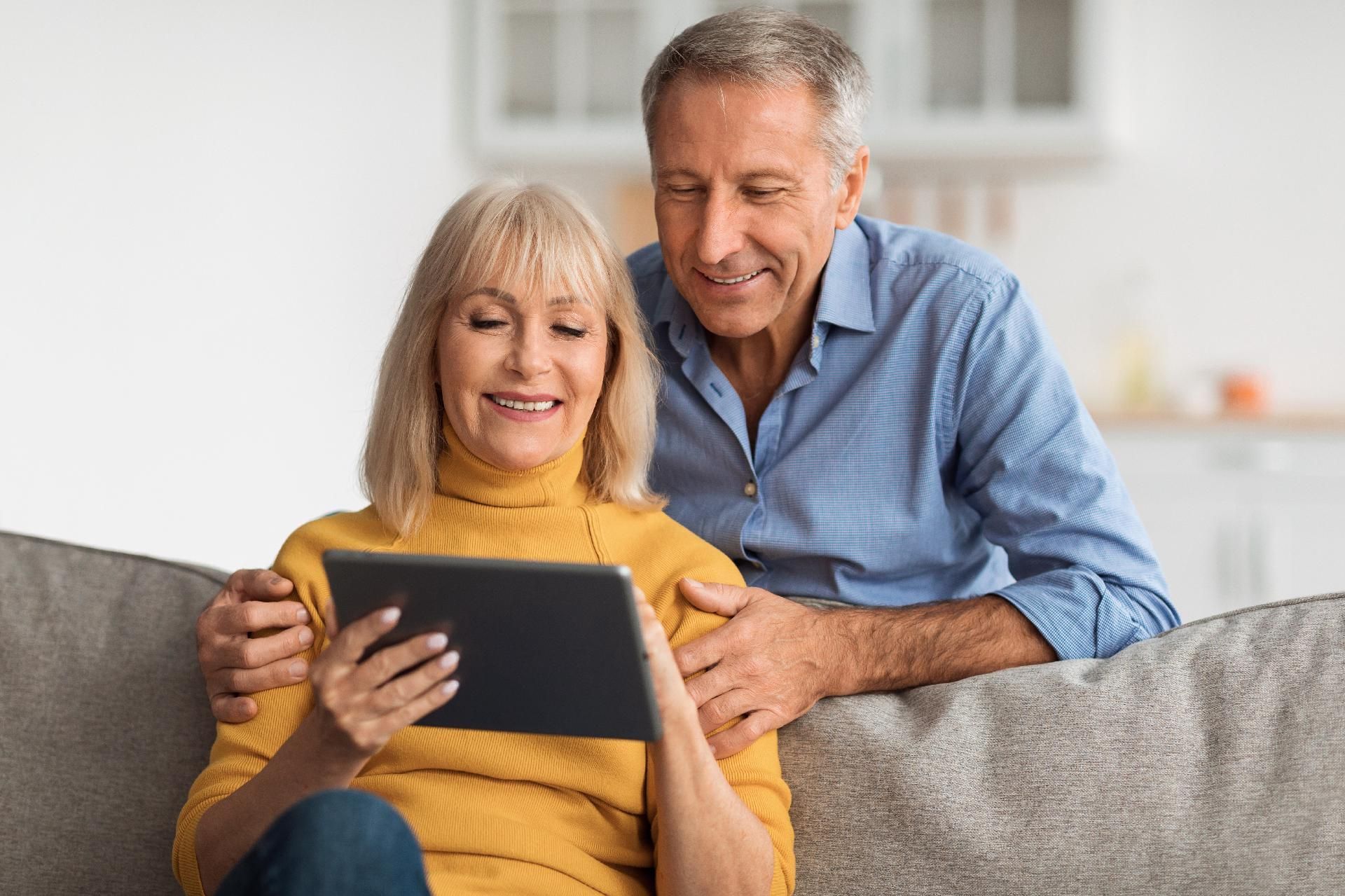 Ein Paar sitzt auf einem Sofa und schaut gemeinsam auf ein Tablet.