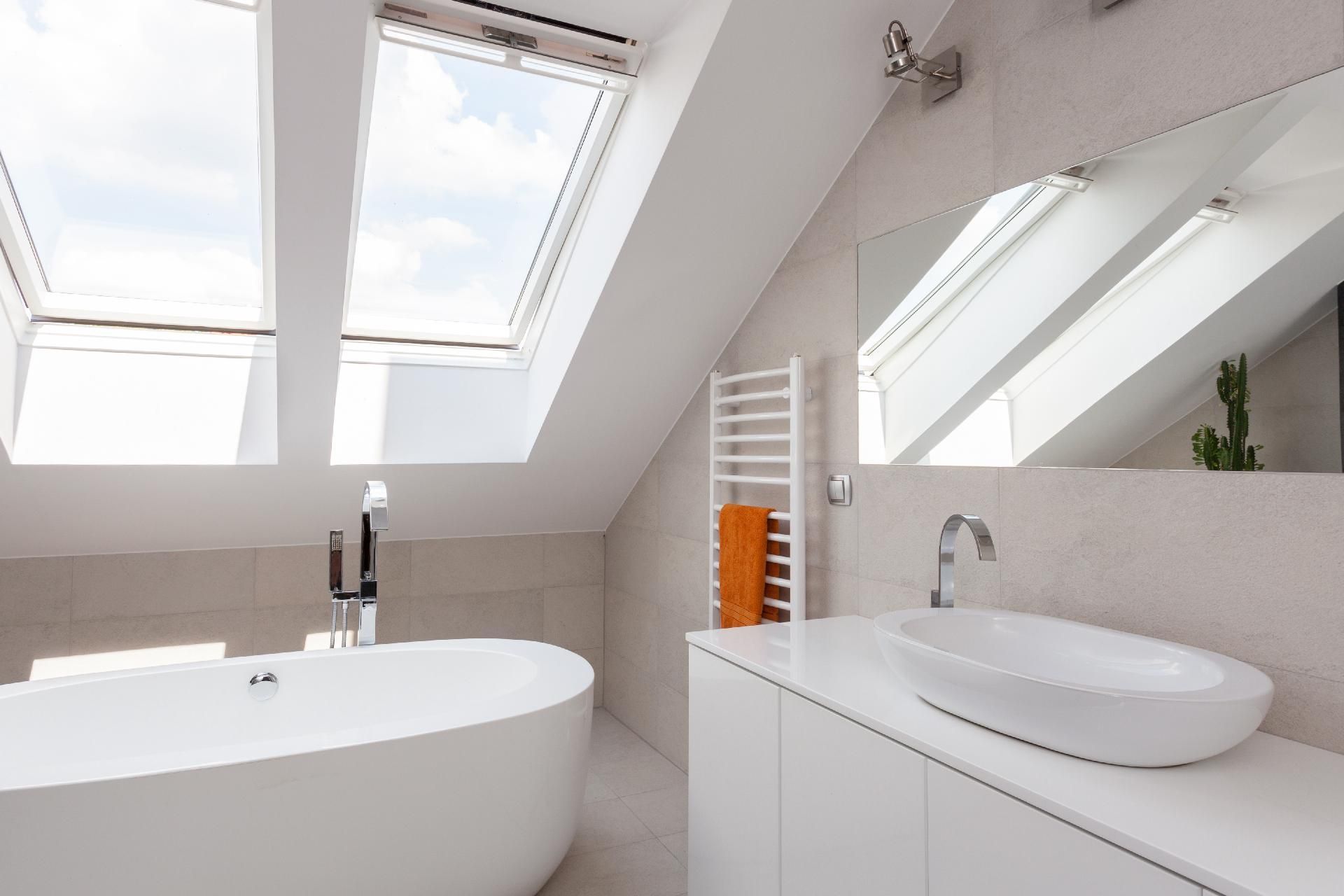 Ein helles Dachgeschossbadezimmer mit einer freistehenden weißen Badewanne, modernen Waschbecken und großen Dachfenstern.