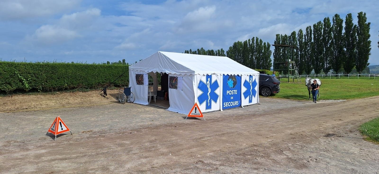 Une grande tente blanche avec des étoiles bleues peintes dessus se trouve au milieu d'un champ de terre.