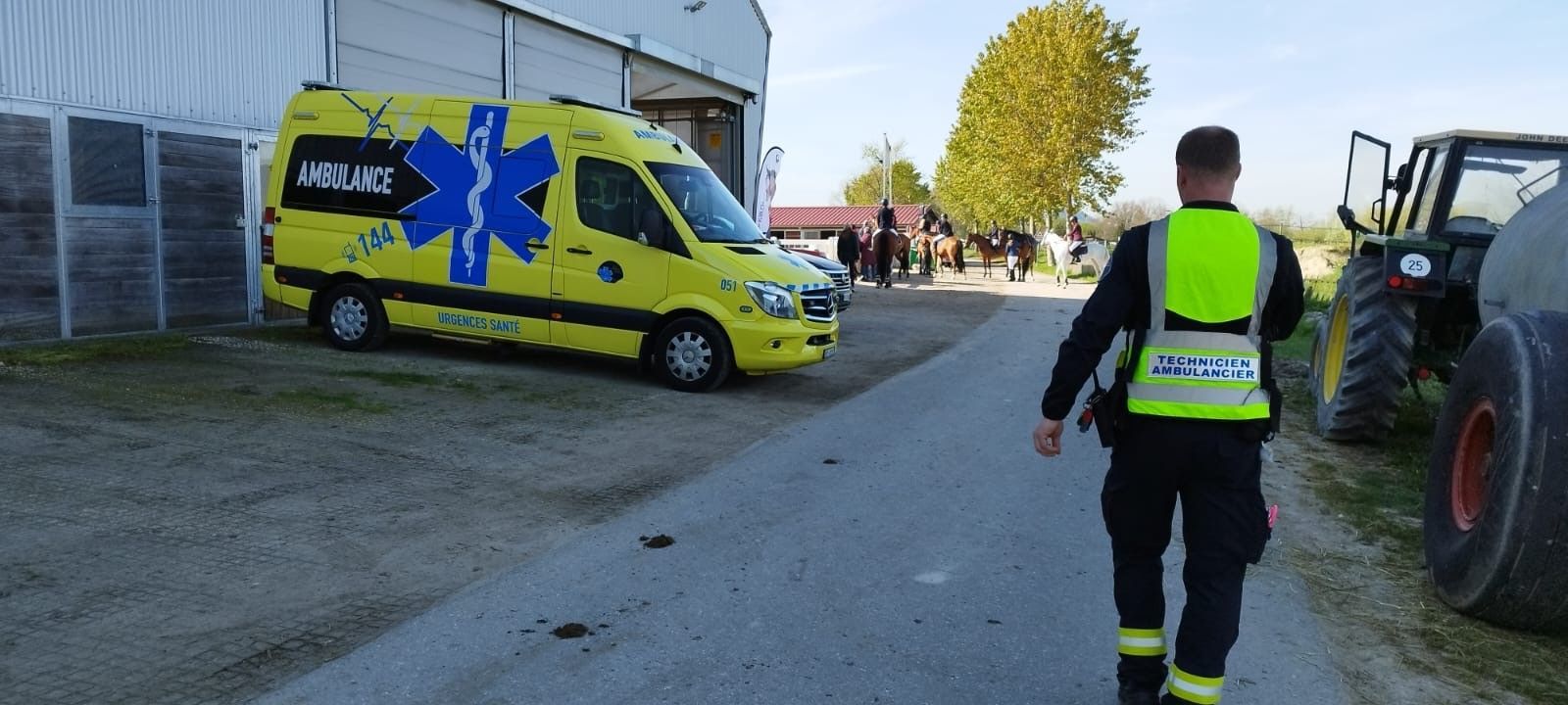 Un homme en gilet jaune marche dans une rue à côté d'une ambulance.