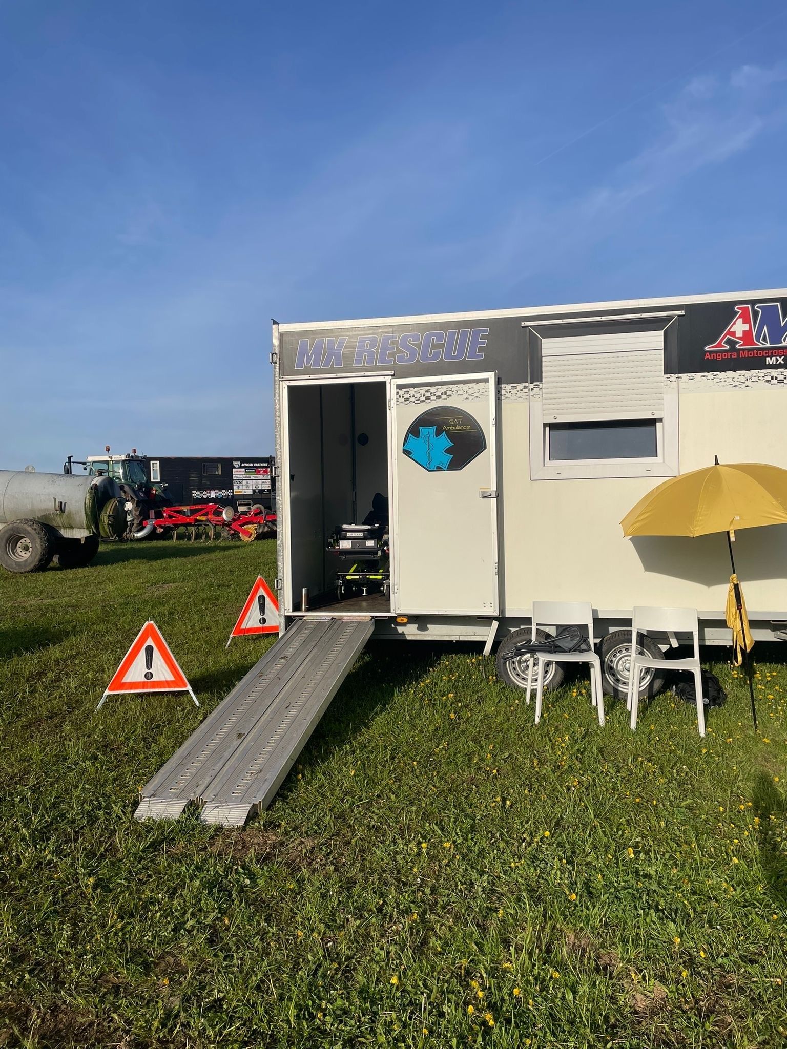 Une remorque avec une rampe et des parapluies est garée dans un champ herbeux.